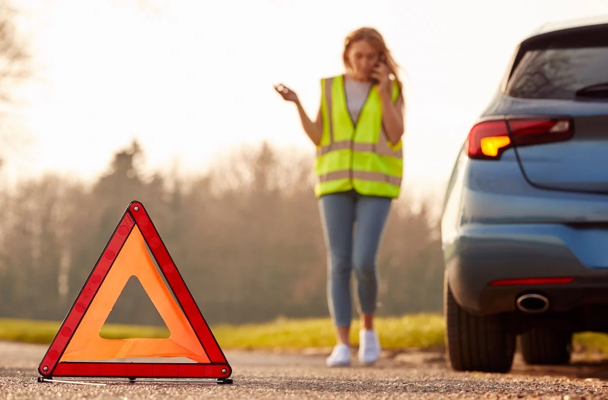 Photo of a car owner making a call on the roadside with her broken down car with hazard warning